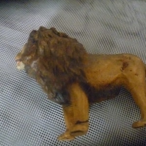 May include: A wooden lion figurine, with a detailed mane and a standing pose. The lion is painted in shades of brown and tan, with visible wood grain. The figurine is a decorative item, likely a collectible or a toy.