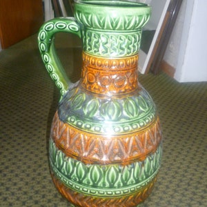 Può includere: Un grande vaso in ceramica verde e marrone con un motivo geometrico. Il vaso ha un'ampia apertura e un manico.