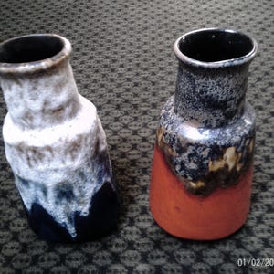 Puede incluir: Dos jarrones de cerámica con acabado texturizado. Un jarrón es blanco, gris y azul marino. El otro jarrón es naranja, negro y gris. Ambos jarrones tienen un interior oscuro y una forma ligeramente inclinada.