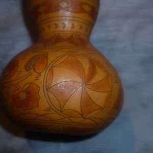 Puede incluir: Una calabaza marrón con intrincados diseños pintados a mano en tonos marrones y naranjas. La calabaza presenta un diseño circular con un patrón de remolino y formas geométricas.