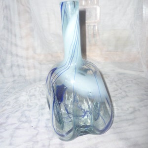 May include: A clear glass vase with a bulbous, multi-lobed base and a slender neck. The glass features swirling white opaque accents and thin, dark blue glass lines that wrap around the body and neck in a spiral pattern.