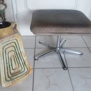 Puede incluir: Un taburete giratorio de cuero marrón con base cromada y cinco patas. El taburete está sobre un suelo de baldosas.