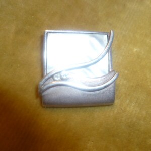 May include: A silver pendant with a white mother-of-pearl inlay and two small clear stones. The pendant is shaped like a wave with a curved design.