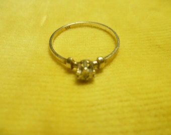 Könnte beinhalten: Ein goldener Ring mit einem kleinen, klaren Stein, der in einem kronenartigen Design gefasst ist. Der Ring ist innen mit "XFX" gekennzeichnet.