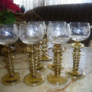 以下が含まれることがあります： エッチングされた花の模様が施された透明なガラス製のワイングラス6個セット。グラスは琥珀色のステムと球根状のベースを持っています。