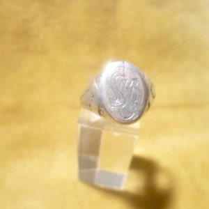 May include: A silver ring with an oval shaped top. The top of the ring has an engraved design of the letters "S" and "B" intertwined.