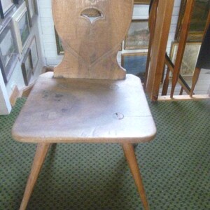 Peut inclure: Une chaise en bois brun clair dotée d'un dossier en forme de cœur avec une découpe sculptée. La chaise possède une assise carrée et plate ainsi que quatre pieds fuselés. Le grain du bois est visible sur toute la surface de l'objet.