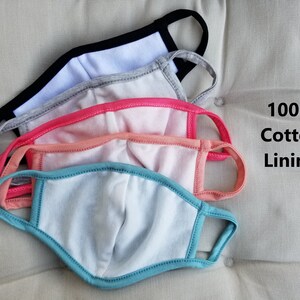 May include: Four face masks stacked on top of each other. The masks are made of a soft, breathable fabric. The top mask is black with a white lining. The second mask is gray with a white lining. The third mask is pink with a white lining. The bottom mask is blue with a white lining. The text "100% Cotton Lining" is visible in the image.