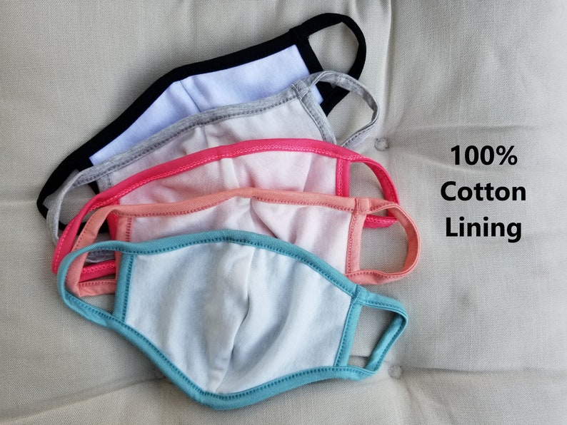 May include: Four face masks stacked on top of each other. The masks are made of a soft, breathable fabric. The top mask is black with a white lining. The second mask is gray with a white lining. The third mask is pink with a white lining. The bottom mask is blue with a white lining. The text "100% Cotton Lining" is visible in the image.
