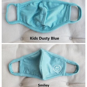 May include: A light blue kids face mask with a white smiley face design. The mask is made of a soft, breathable fabric.