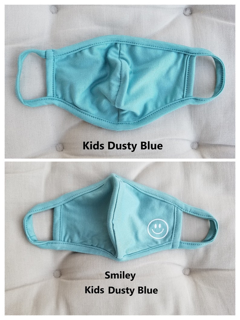 May include: A light blue kids face mask with a white smiley face design. The mask is made of a soft, breathable fabric.