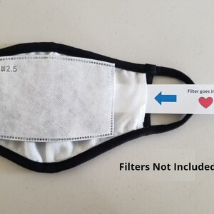May include: Black face mask with a white filter pocket labeled "PM2.5". A blue arrow points to the filter pocket with a red heart and the text "Filter goes in here". The text "Filters Not Included" is printed below the mask.