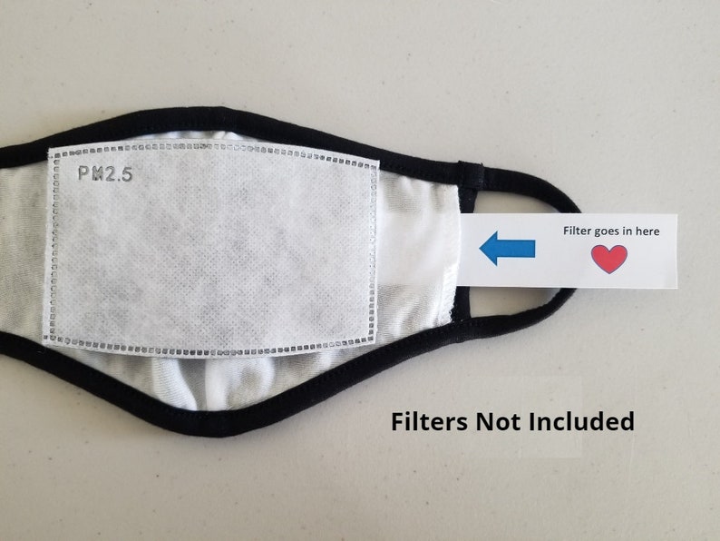 May include: Black face mask with a white filter pocket labeled "PM2.5". A blue arrow points to the filter pocket with a red heart and the text "Filter goes in here". The text "Filters Not Included" is printed below the mask.
