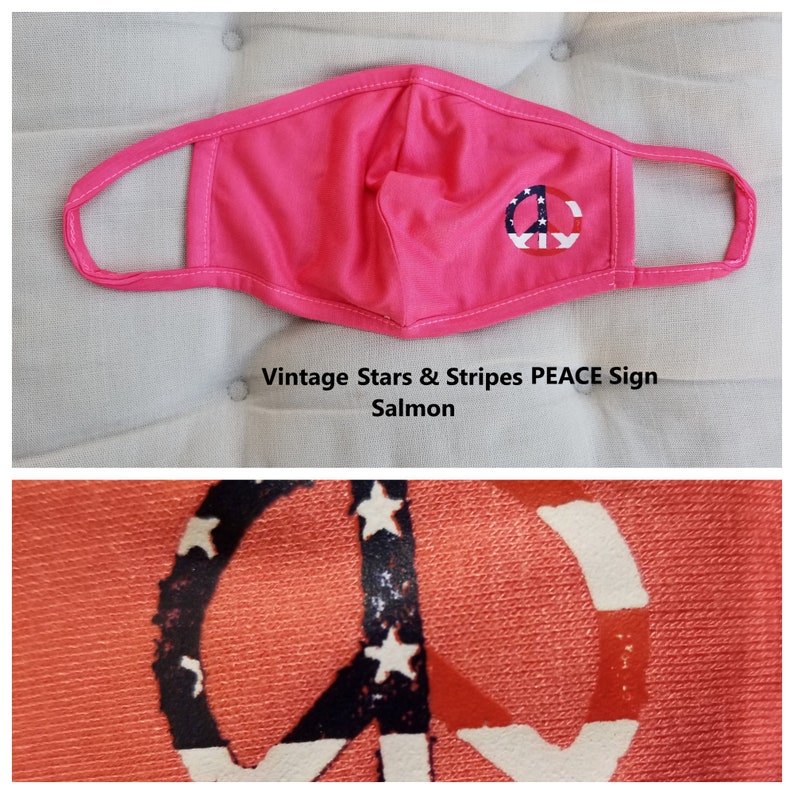 Puede incluir: Una mascarilla facial rosa con un s&iacute;mbolo de paz impreso en ella. El s&iacute;mbolo de paz est&aacute; formado por estrellas y rayas rojas, blancas y azules. El texto "Vintage Stars & Stripes PEACE Sign Salmon" est&aacute; impreso debajo de la mascarilla.