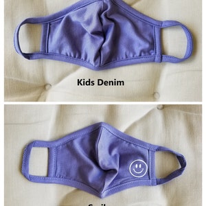 May include: Two purple face masks with elastic ear loops. The top mask is plain. The bottom mask has a white smiley face on the right side. Both masks are labeled "Kids Denim".