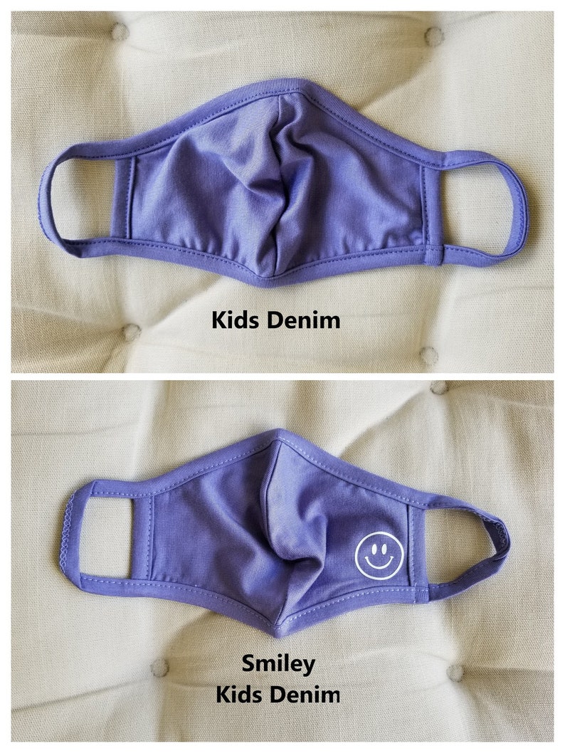 May include: Two purple face masks with elastic ear loops. The top mask is plain. The bottom mask has a white smiley face on the right side. Both masks are labeled "Kids Denim".