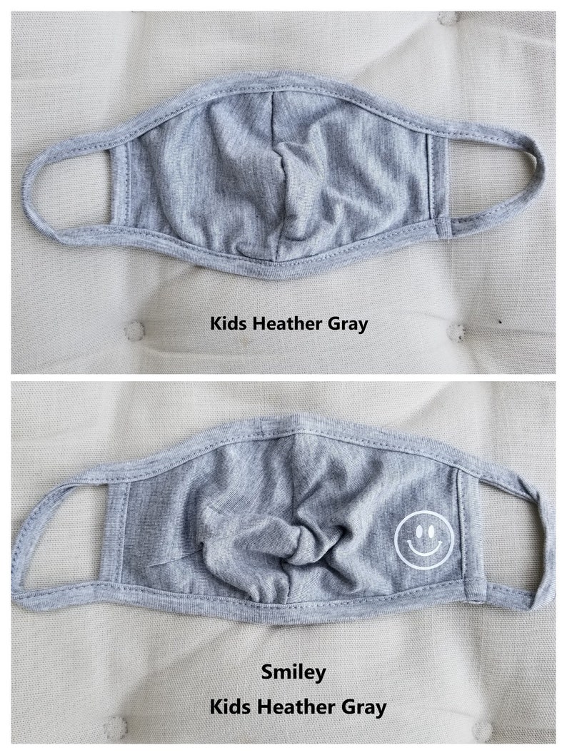 May include: Two gray face masks for kids. The top mask is plain, while the bottom mask has a white smiley face design. Both masks are labeled "Kids Heather Gray".