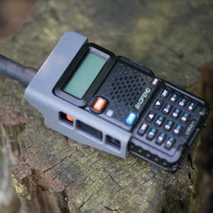 May include: A gray and black handheld two-way radio with a black antenna, a screen, and a keypad. The radio has the word "Baofeng" printed on the side.