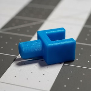 May include: A blue plastic connector piece with a U-shaped opening. The connector has a smooth, slightly textured surface.