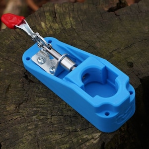 May include: A blue plastic clamp with a silver lever and a red handle. The clamp is designed to hold objects securely.
