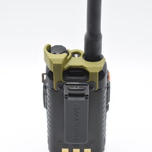May include: A black handheld two-way radio with a black antenna and a green clip. The radio has the word "BAOFENG" printed on the front. The radio is on a white background.