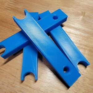 May include: A collection of bright blue, rectangular plastic pieces. Each piece has a curved notch on one end and a hole near the other. The pieces are stacked and slightly overlapping on a wooden surface.