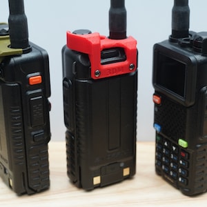 May include: Three black handheld radios with different colored accessories. The radio on the left has a green accessory, the middle radio has a red accessory, and the radio on the right has a black accessory.