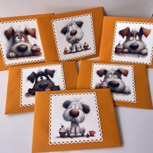 May include: A collection of six greeting cards featuring cartoon dogs with cupcakes. Each card has a unique dog illustration within a white, scalloped border, set against a mustard-yellow envelope. The dogs have various fur colors and expressions.