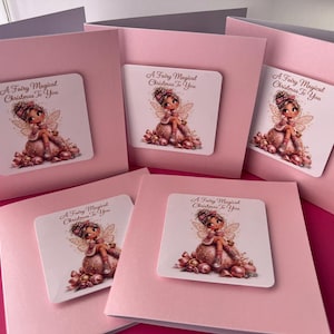 May include: Five square light pink greeting cards featuring a central white square insert. Each insert displays a cartoon fairy sitting on a large ornament with the text A Fairy Magical Christmas To You printed in a dark brown script font.