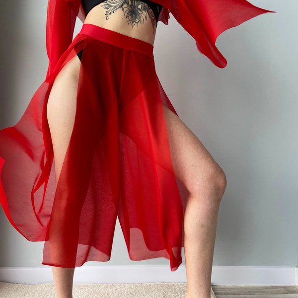 May include: A flowing red skirt with high slits and matching long-sleeved top. The sheer fabric drapes elegantly, creating a dynamic silhouette. The outfit is a vibrant shade of red, perfect for dance or performance wear.