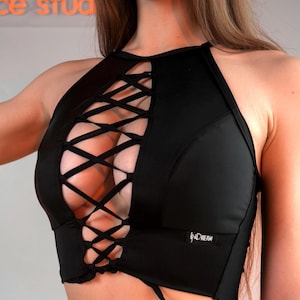 May include: A black sleeveless crop top featuring a high neckline and a central vertical cutout with a crisscross lace-up closure. The garment includes a small rectangular label on the lower right side with the text INDREAM printed in white.