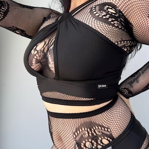 Puede incluir: Conjunto de lencer&iacute;a negra con top halter con tirantes cruzados y braguita de cintura alta a juego. El conjunto incluye mangas largas y detalles de red con un estampado floral. La marca "INDREAM" es visible en la cintura.