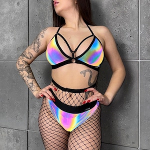 以下が含まれることがあります： 虹色の反射素材を使用した、ツーピースのビキニセット。 トップはホルターネックで、黒いストラップとリングのディテールが特徴です。 ハイウエストのボトムは黒いウエストバンドが付いています。 黒のフィッシュネットストッキングと合わせています。