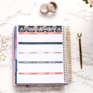 May include: A white planner with a gold spiral binding. The planner has a black and white patterned cover with the text "Weekly Check-ins". The planner is open to a page with the headings "Week 1", "Category", "Spent", and "Remaining".