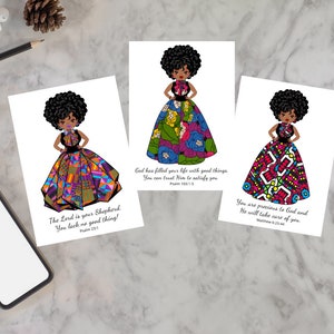 May include: Three greeting cards featuring illustrations of a woman in colorful dresses. Each card has a different dress design and a Bible verse. The cards are on a marble surface.