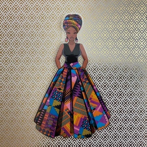 Op de afbeelding: Een vrouw draagt een kleurrijke, gepatroneerde rok en een zwart topje met een hoofddoek. De rok heeft een geometrisch patroon in tinten van paars, oranje, blauw en geel.
