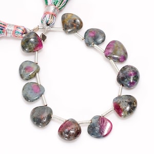 Pode incluir: Um fio de contas de pedras preciosas em forma de coração. As contas são uma mistura de verde, cinza e rosa.