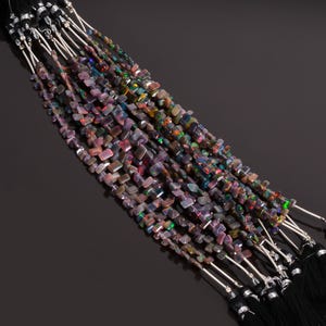 May include: Strands of black opal gemstone beads with iridescent flashes of color. The beads are small, rectangular, and strung together with silver-colored wire. Each strand ends with a black tassel.