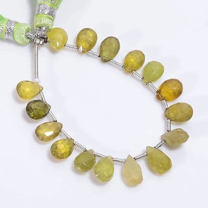 Puede incluir: Hilo de piedras preciosas facetadas en forma de lágrima, en tonos amarillos y verdes. Las cuentas están ensartadas en un alambre plateado, con una borla verde en la parte superior. Las piedras varían en color.