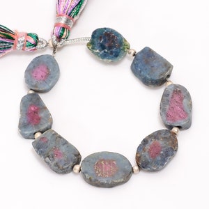 May include: A strand of blue and pink gemstone beads with silver spacers. The beads are oval shaped and have a rough, natural texture. The strand is finished with a colourful tassel.