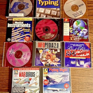 May include: A collection of eleven assorted computer software CD-ROM cases arranged in a grid. Titles include Typing, Musical Instruments, Need for Speed III, Compton's 3D World Atlas, Infopedia 2.0, God Bless America, War Birds, and Flying High.