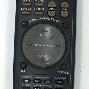 May include: A black Samsung remote control with a circular button in the center. The button has the words "PLAY", "REW", "F.F", and "STOP" printed on it. The remote has a variety of buttons, including "VCR POWER", "TV POWER", "SELECT", "MUTE", "ENTER", "PROG", "VOL", "CH", "REPEAT", "SLOW", "F.ADV/SKIP", "SP.SLP", "TRACKING", "INDEX", "EJECT", "CLEAR DISPLAY", "AUDIO", "RESET", and "633-104".