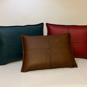 May include: Three decorative throw pillows with a stitched design. The pillows are made of leather and are in the colors green, brown, and red.