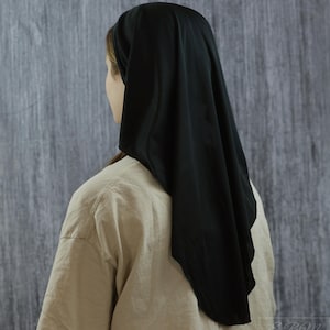 May include: A solid black head covering worn over the hair, featuring a smooth, lightweight fabric that drapes down the back of the head. The head covering is styled in a simple, plain design with no patterns, textures, or additional embellishments.