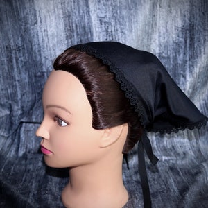 May include: Black fabric head covering with a lace trim and a black ribbon tie. The head covering is worn on a mannequin head with brown hair.