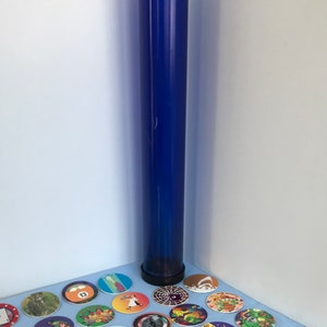 May include: A blue plastic tube with a black cap, surrounded by a collection of colorful round game pieces with various designs and numbers.
