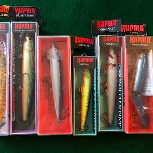 May include: A collection of seven Rapala fishing lures in various colors and styles, including the Husky Jerk, Original, and Jointed Articulated models. The lures are displayed in their original packaging.