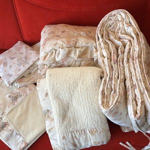 May include: A set of cream-colored bedding with a floral pattern. The set includes a comforter, pillowcases, and a blanket.