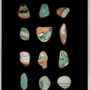 Puede incluir: Una colección de 12 pequeñas baldosas de cerámica de forma irregular con patrones verdes, blancos y naranjas. Las baldosas están dispuestas en una cuadrícula sobre un fondo negro.