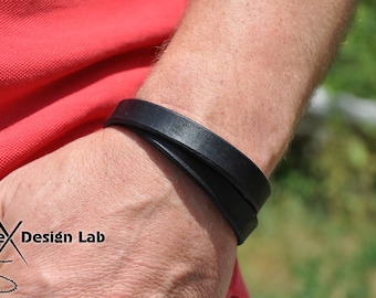 May include: A black leather bracelet with two straps wrapped around the wrist. The bracelet is made of a thick, durable leather and has a simple, elegant design.